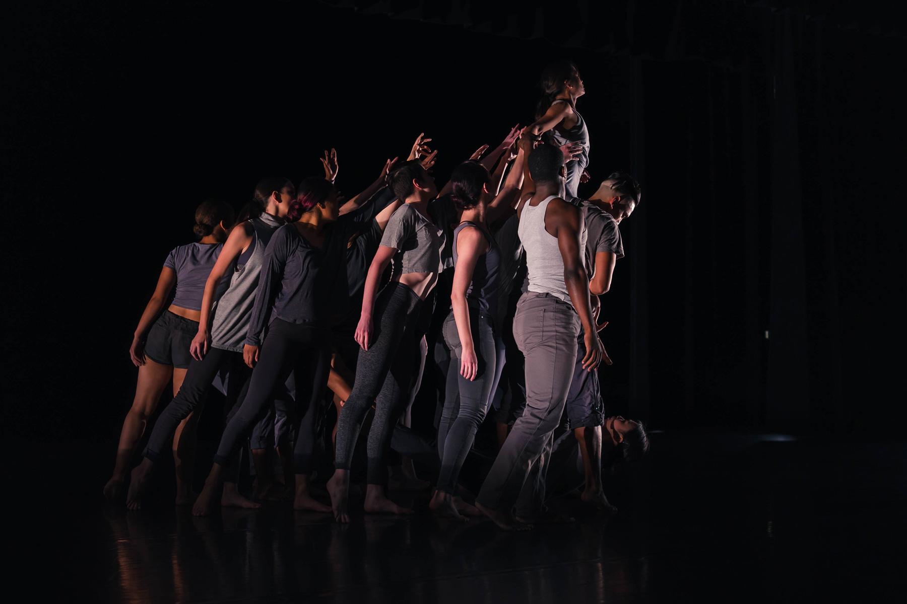 跳舞 students under a bright spotlight in a dark stadium pose tightly together on stage.